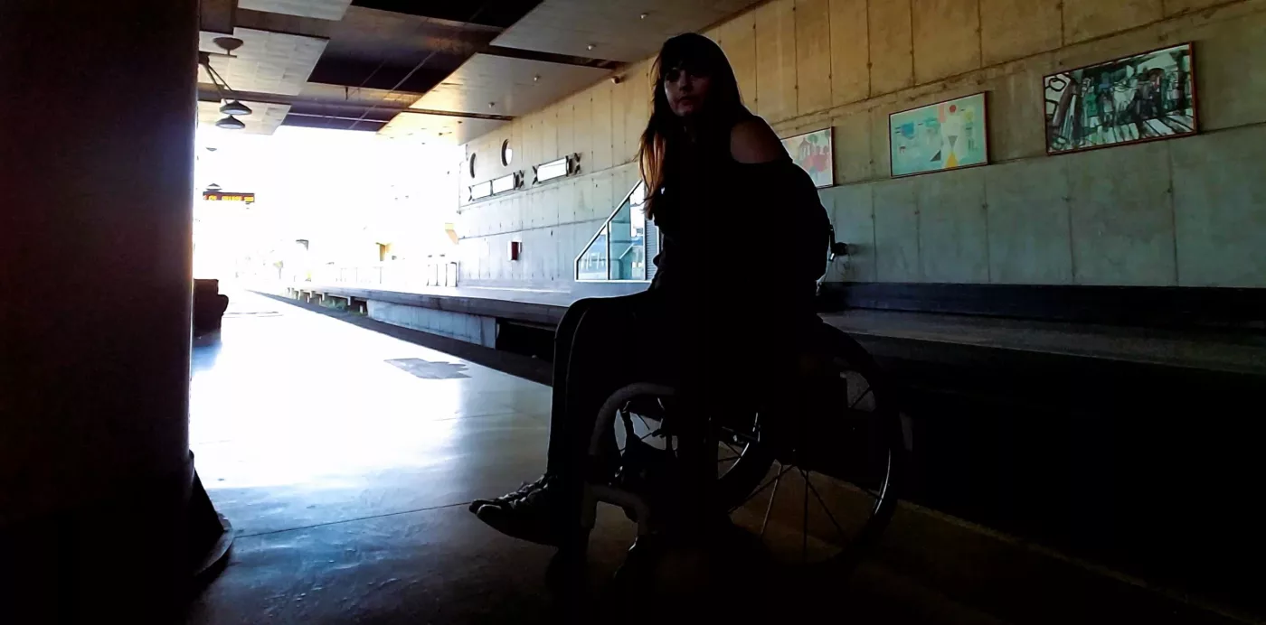 A silhouette of woman in a manual wheelchair waiting at a train station.